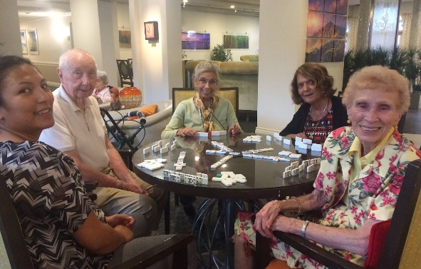 Residents and a caregiver enjoying a game of dominoes together