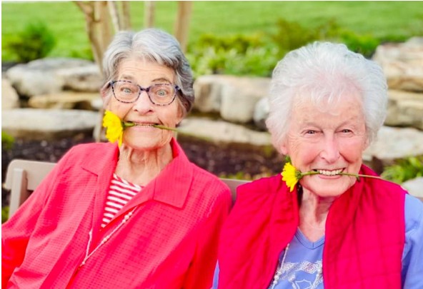 Two joyful senior women smiling outdoors, each holding a flower